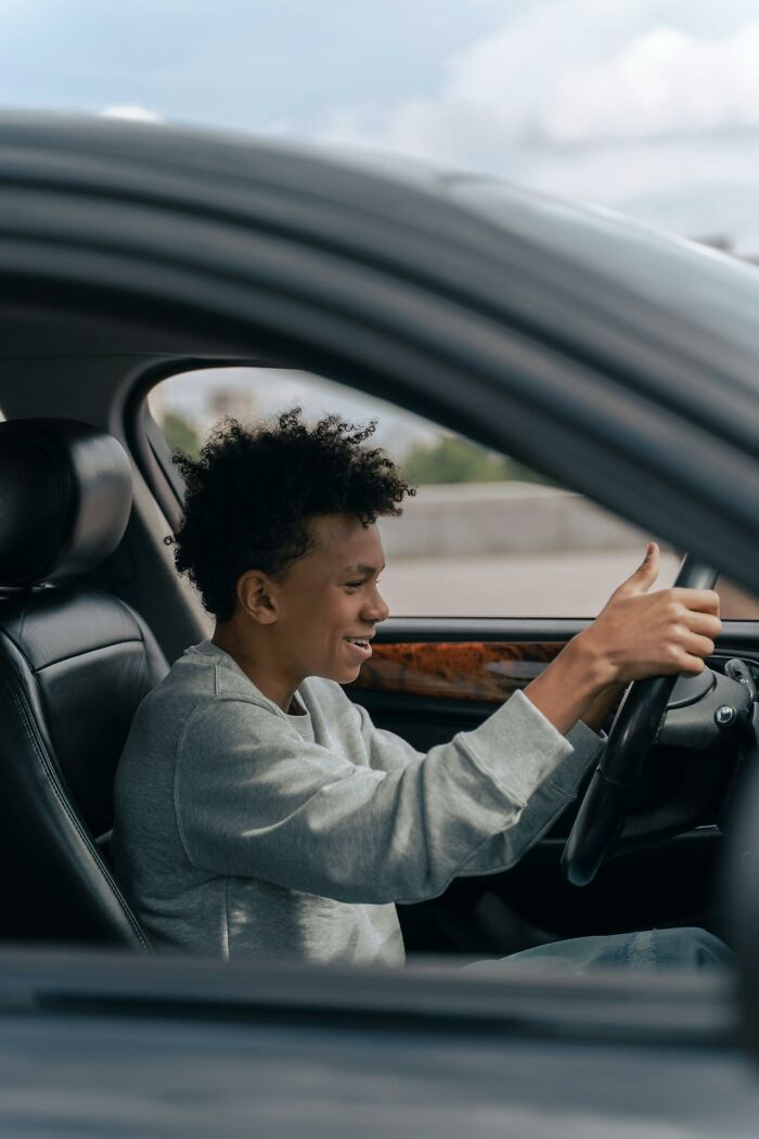 Teen boy smiling while driving a car, capturing a heartwarming and harmless secret moment inside the vehicle.
