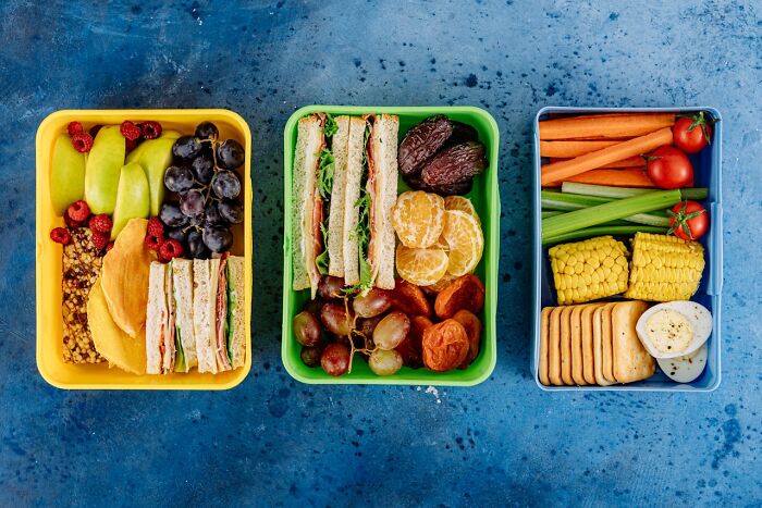 Three lunch boxes with sandwiches, fruits, and vegetables packed neatly for teens by caring parents. - 32