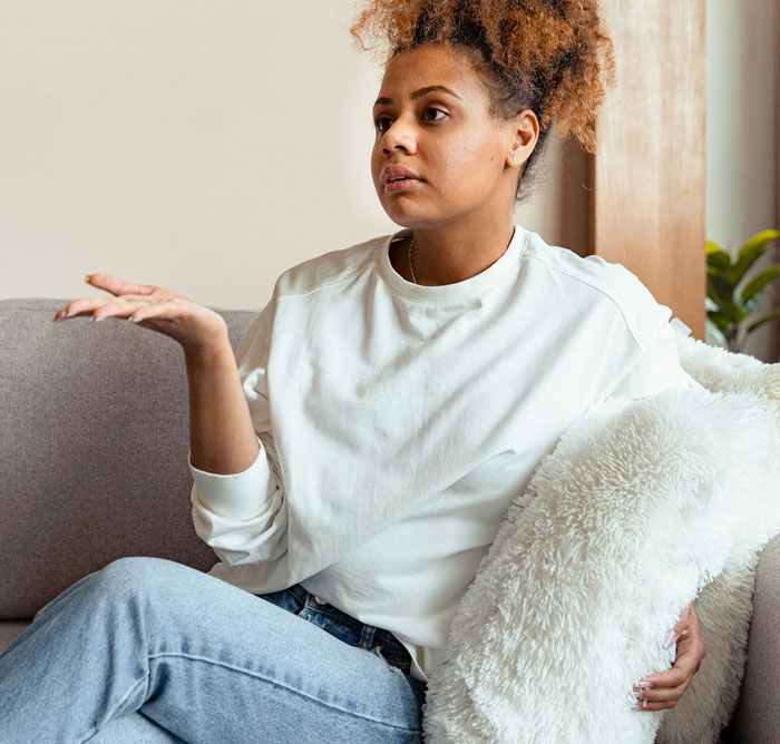 Young woman sitting on couch looking frustrated, illustrating friend breaks into house and plants belongings to prove residence.