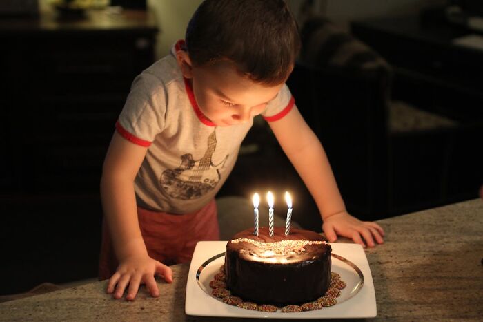Young boy leaning over a table, blowing out candles on a birthday cake, capturing heartwarming secrets moment.