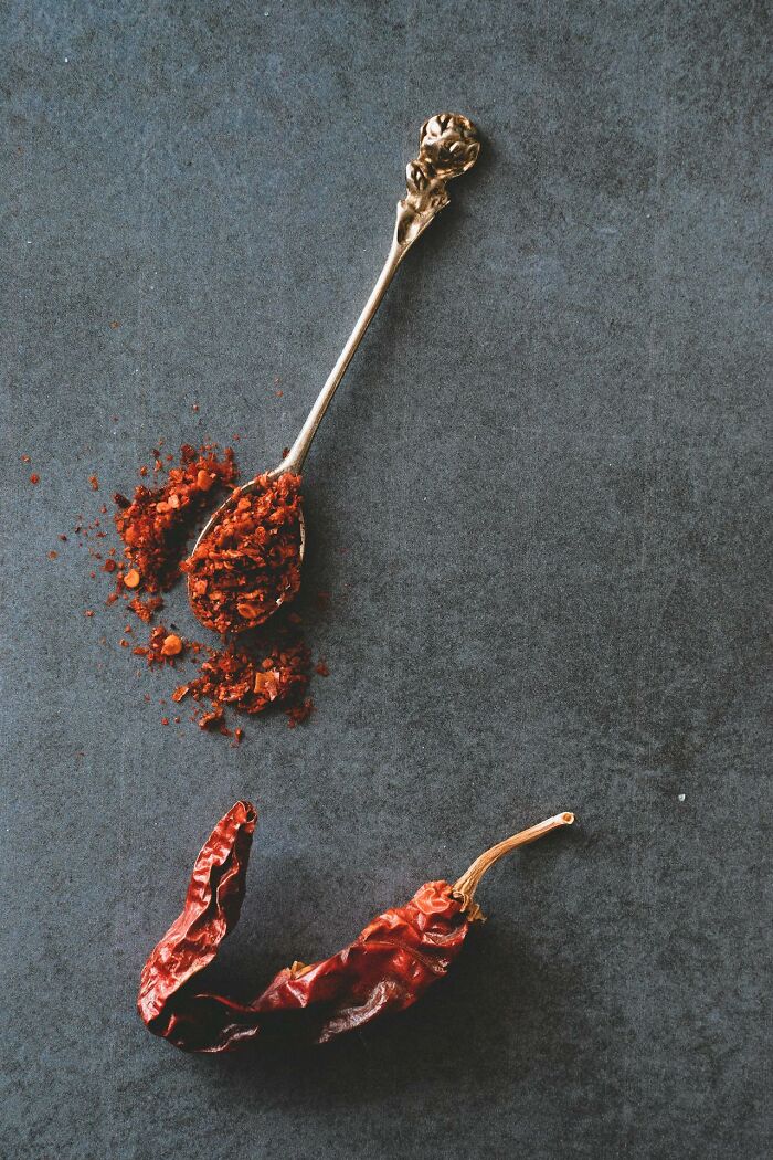 Dried chili pepper and crushed chili flakes on a vintage spoon against a dark textured background.