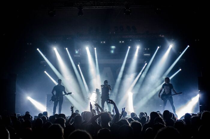 Live band performing on stage with bright lights and a large crowd, illustrating heartwarming secrets shared openly.