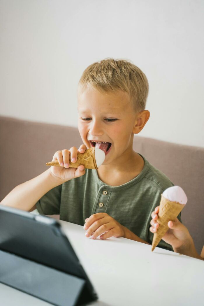 Young boy eating ice cream while watching a digital tablet, illustrating kids' imaginary friends and creepy experiences.