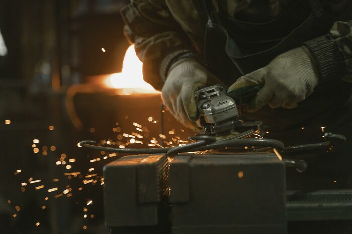 Person wearing gloves using a grinder on metal with sparks flying, illustrating picking the wrong line at the grocery store.