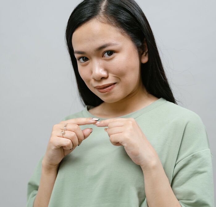 Young woman with long black hair in a green shirt making a small gesture, illustrating picking the wrong line at the grocery store.