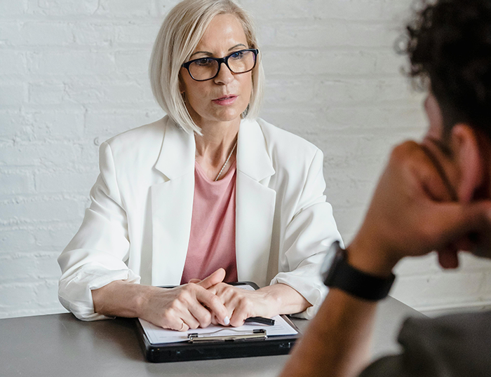 Woman in white blazer disciplinarian worker in a serious discussion with a man at office table about workplace behavior