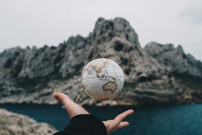 Hand tossing a globe showing Australia and nearby countries with mountains and water in the background travel challenge concept