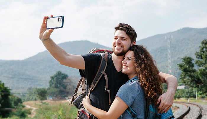 Couple hiking outdoors taking a selfie, capturing a moment before the girlfriend cancels her dream vacation due to work.