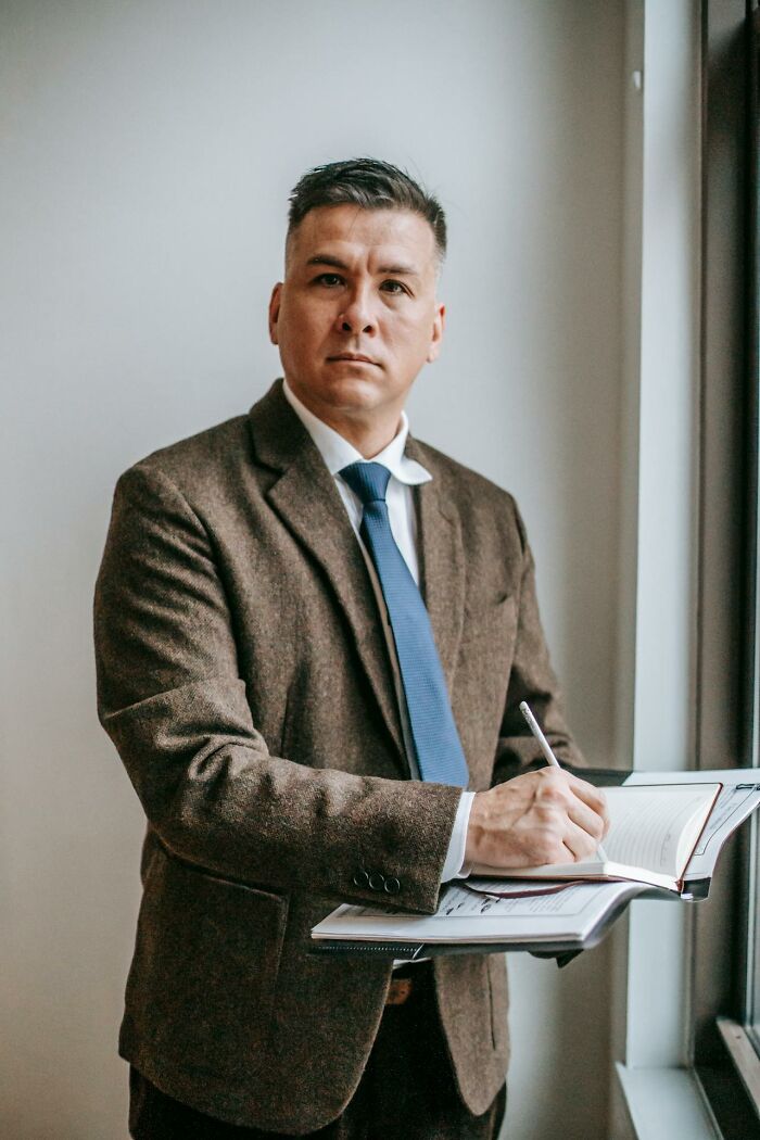 Man in a brown blazer and blue tie writing in a notebook by the window illustrating talking to a psychopath concept