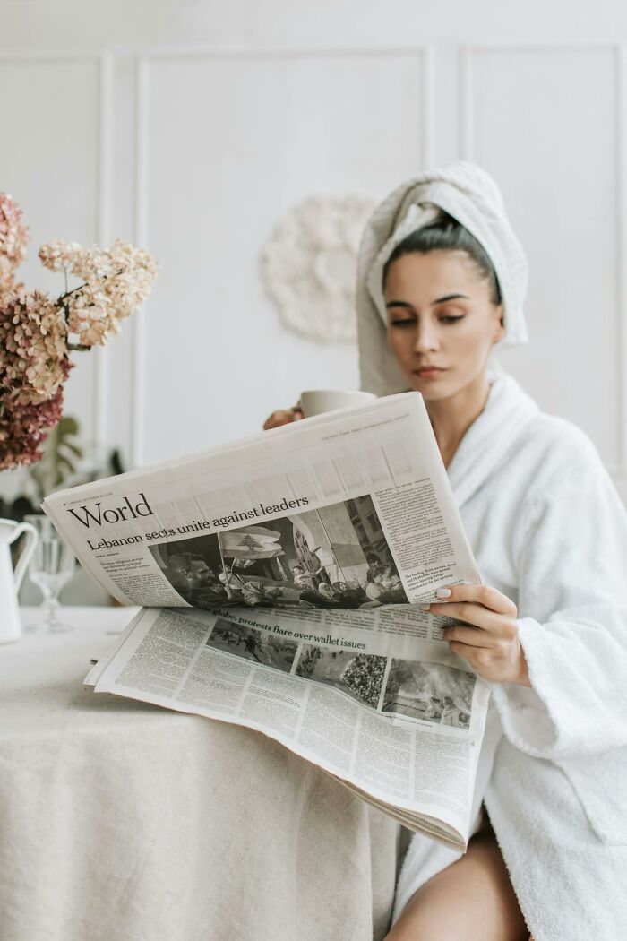 Woman in a bathrobe with a towel on her head reading a newspaper and holding a cup, relaxing in a calm setting about surviving crazy situations.