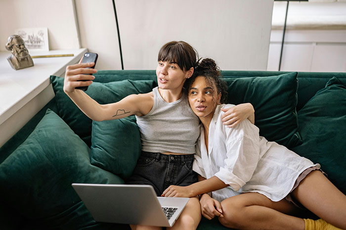 Two women sitting closely on a sofa taking a selfie, reflecting a moment before dinner chaos involving racist insults.