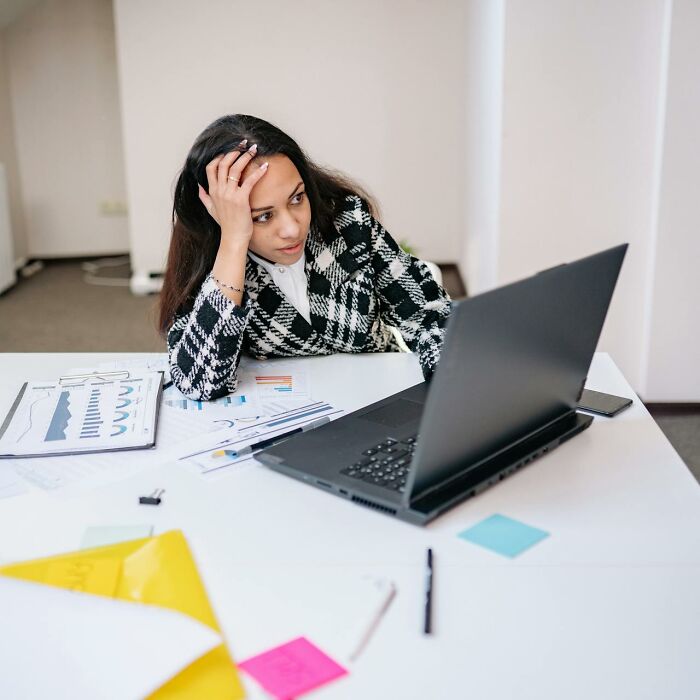 Stressed woman in checkered blazer reviewing documents and laptop, highlighting job interview red flags and toxic workplace signs.