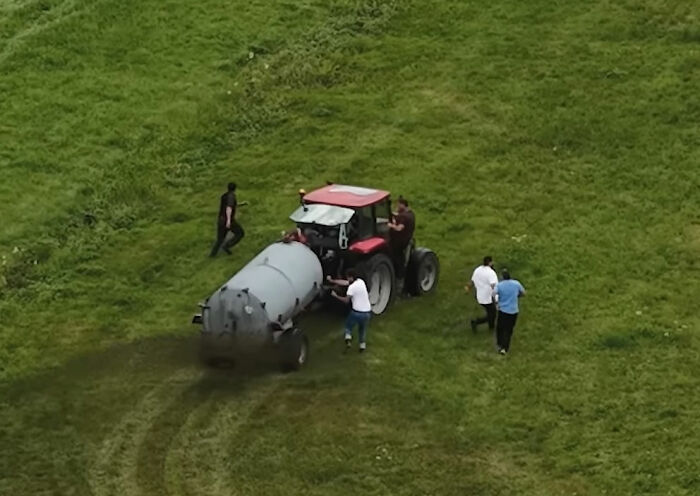 Farmer spraying manure from tractor on grassy field as people walk nearby in viral squatter incident captured by photographer