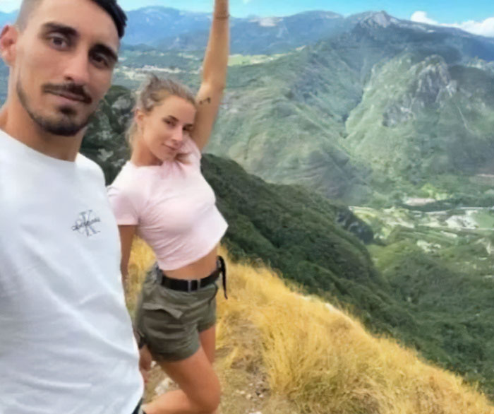 Couple posing for photos taken before disaster with mountains and valley in the background during a sunny day.