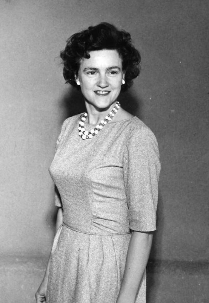 Black and white photo of an LA woman from 1962 in a dress and pearl necklace smiling and posing against a plain background.