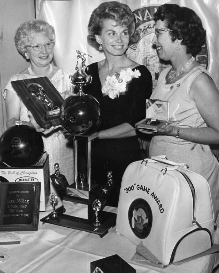 Three LA women in 1962 celebrating with trophies and awards at a bowling event, smiling and dressed in vintage attire.