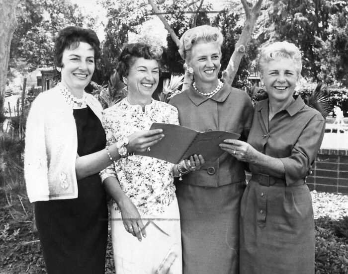 Four LA women smiling and holding a photo album outdoors, enjoying life in 1962.