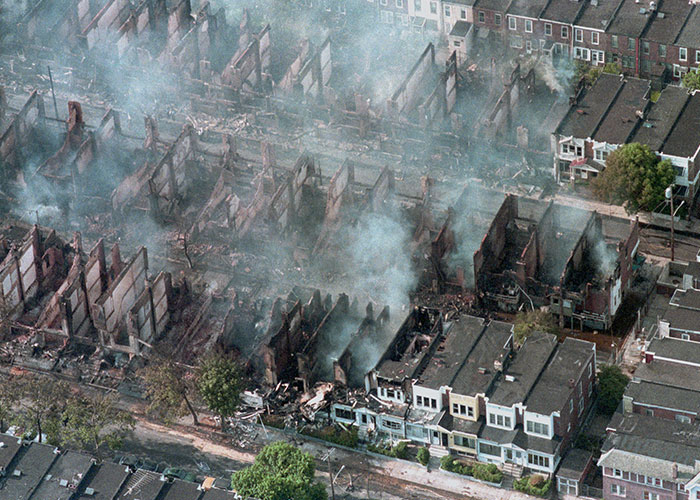 Aerial view of burning row houses with smoke rising, showing historical impact on society by common folk.