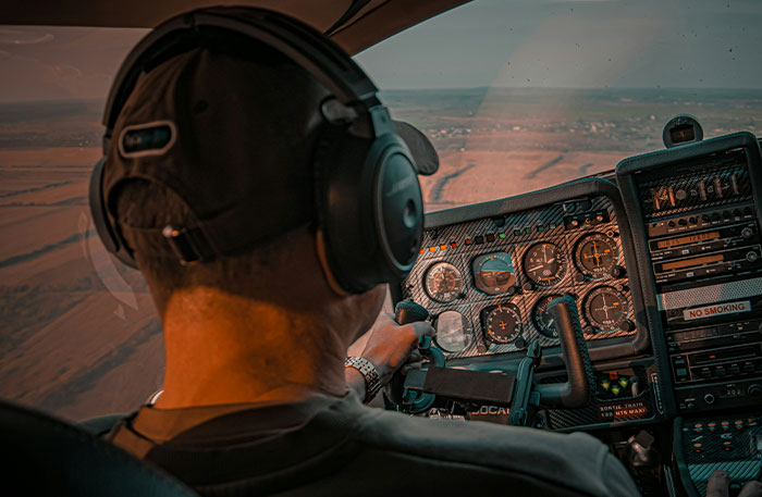 Pilot wearing headset and cap flying a small aircraft, focusing on cockpit instruments and controls during flight.