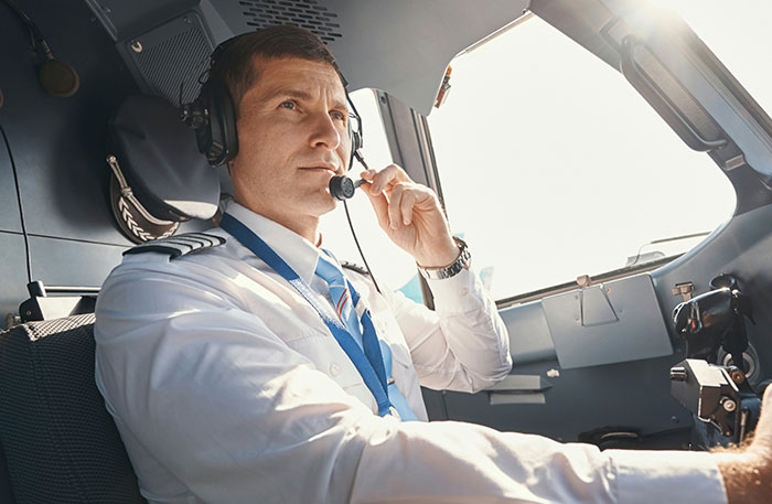 Pilot in cockpit wearing headset and uniform, communicating during a potentially terrifying situation in flight.
