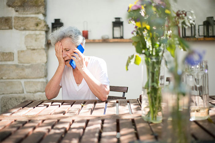 Elderly woman looking distressed while talking on the phone, illustrating memorable wild situations cops handled.