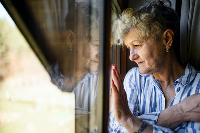 Older woman looking thoughtfully out the window, reflecting quietly on memorable wild situations cops had to deal with.