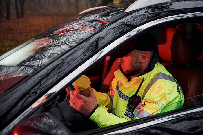 Police officer in a high-visibility jacket sitting in a car, holding a cup, illustrating memorable wild situations cops face.