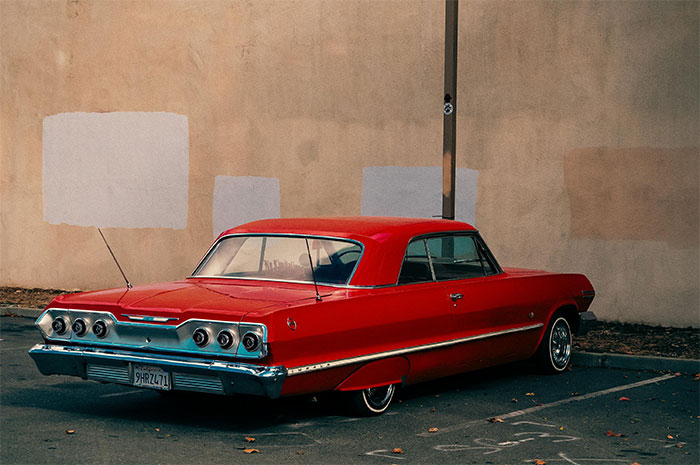 Red vintage car parked by a wall, evoking memorable wild situations cops had to deal with in unique stories.