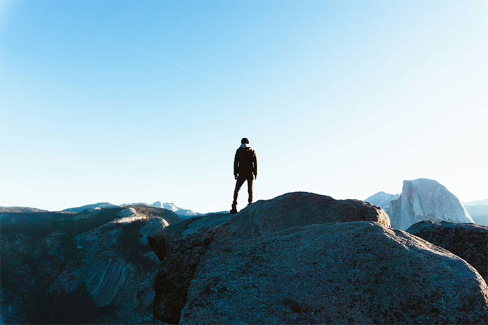 Person standing on a large rock overlooking a vast mountainous landscape at sunrise, illustrating wild situations cops face.