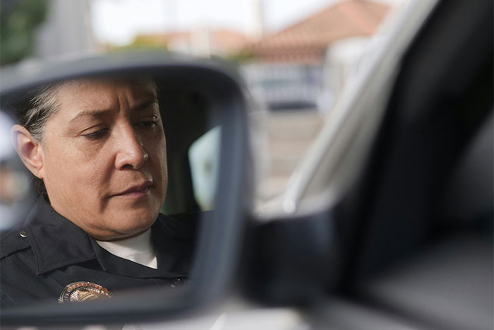 Police officer reflecting in car side mirror, representing memorable wild situations cops had to deal with.