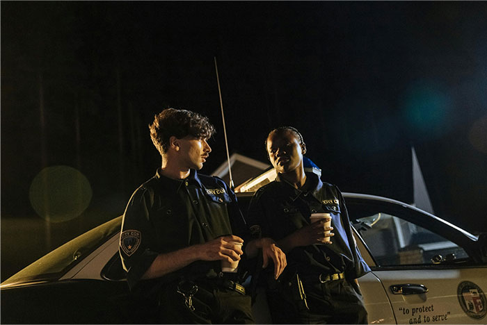 Two police officers in uniform leaning on a patrol car at night after handling wild situations.