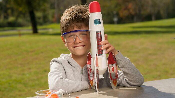 Teenager wearing safety goggles smiling outdoors while holding a model rocket, symbolizing police concerns about illegal activities.