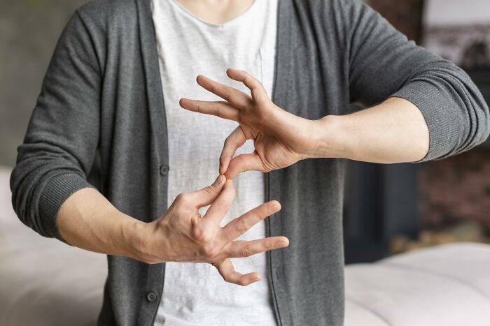 Person in a gray cardigan and white shirt making hand signs related to police and teenagers involved in illegal activities.