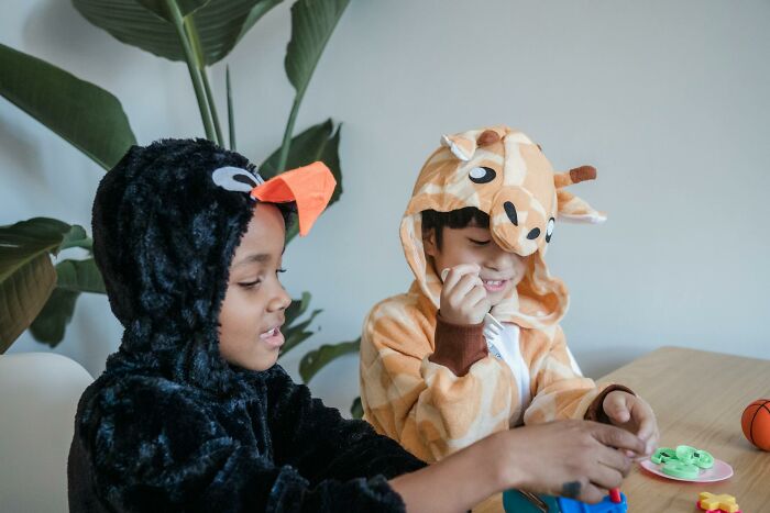 Two kids dressed in animal costumes playing together at a table, showing teenagers' playful interaction indoors