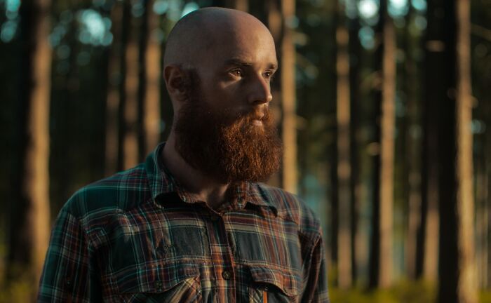 Bearded man in a plaid shirt standing in the woods, reflecting the eerie feeling of sleepless nights after time spent outdoors. - 6