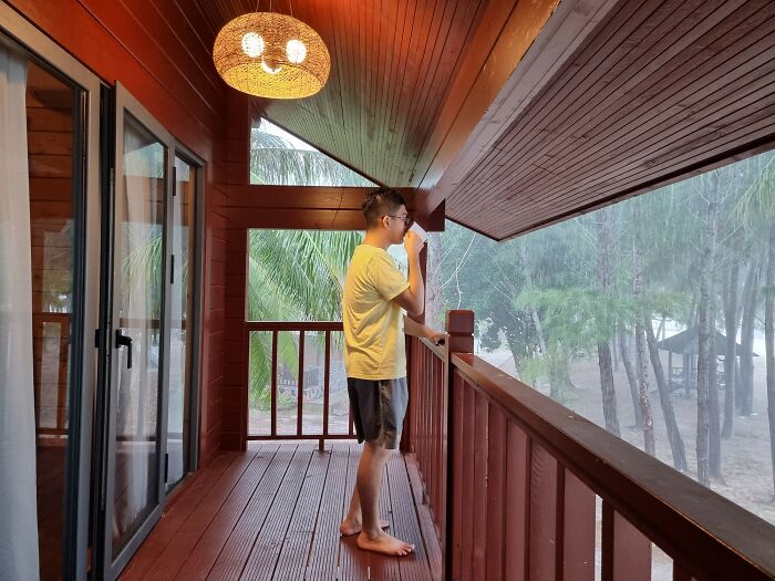 Man standing on a wooden porch, looking out at the rainy woods, reflecting a peaceful yet eerie forest atmosphere. - 13