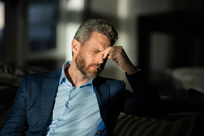 Stressed man sitting alone in dim room, reflecting on ultimatum after caring dad lets pregnant daughter move back home.