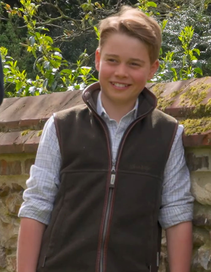 Prince George outdoors smiling, wearing a brown vest and plaid shirt during a casual moment in the Greek Isles. Prince George outdoors smiling, wearing a brown vest and plaid shirt during a casual moment in the Greek Isles.