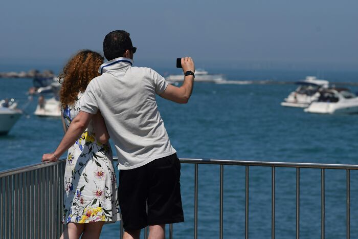 A couple taking a selfie by the waterfront, illustrating common performative behaviors in society.