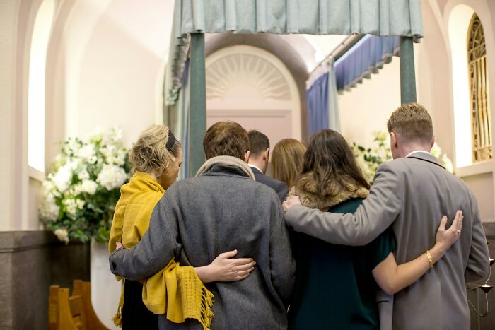 A group of people embracing in a solemn setting, illustrating performative behaviors and social interactions in society.
