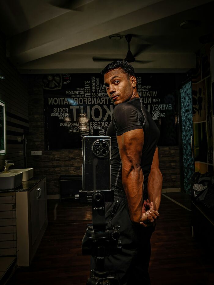 A muscular man posing in a gym, highlighting performative behaviors related to fitness and societal expectations.