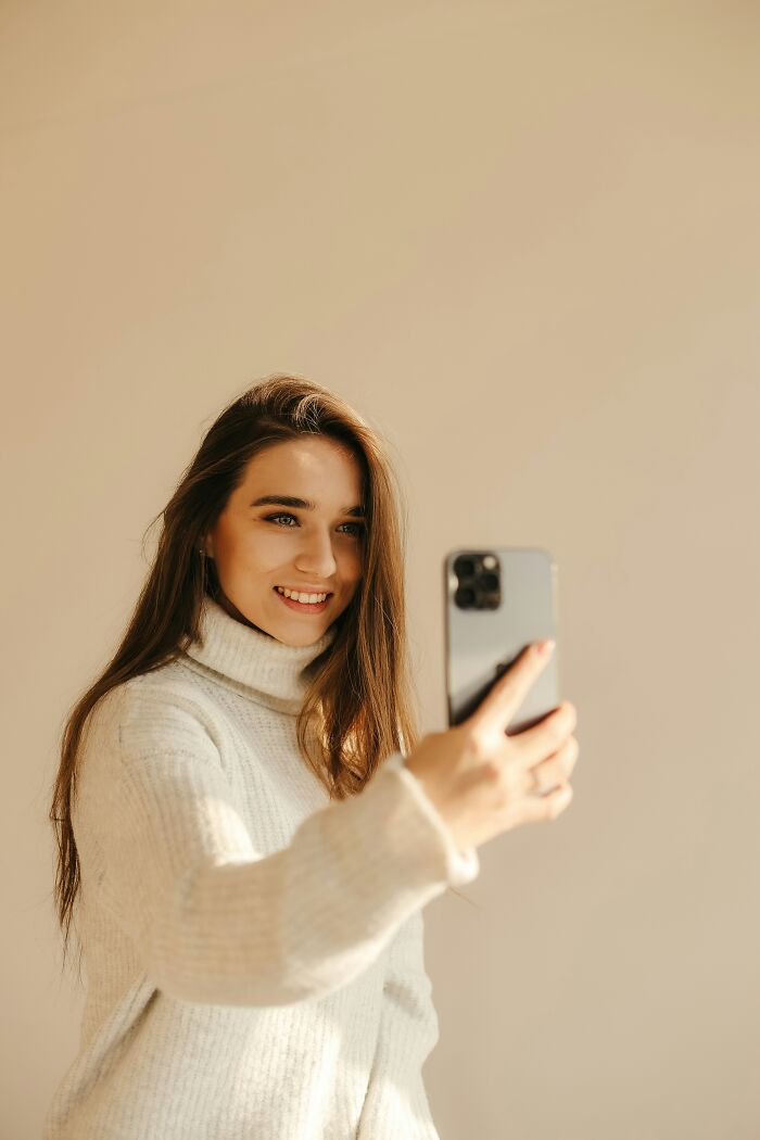 Young woman in a white sweater taking a selfie, illustrating common performative behaviors in modern society.
