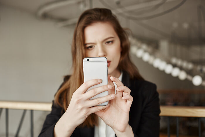 Young woman focused on her smartphone, experiencing intense reactions while browsing Reddit, not for the faint of heart.