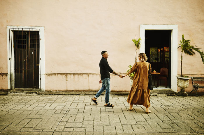 Couple holding hands walking along a street beside a pastel wall, capturing mood-based questions for crush moments.