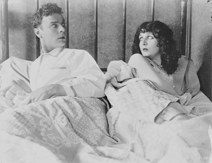 Black and white photo of a surprised couple in bed, perfect for mood-based questions to ask your crush concept.