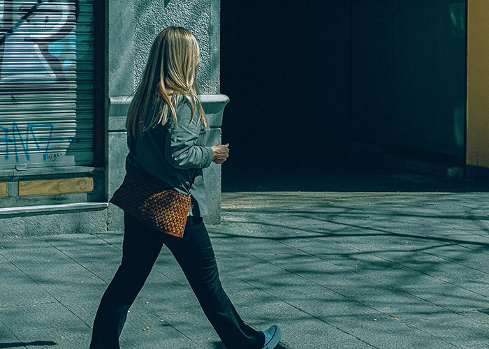 Woman walking on city sidewalk near building with graffiti, illustrating quick reactions preventing tragedy in urban setting.