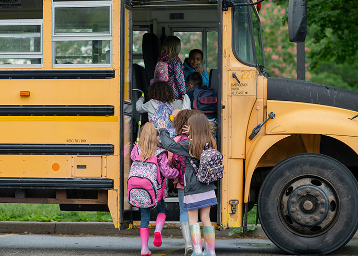 Children boarding a school bus with backpacks and rain boots, illustrating quick reactions preventing a tragedy scenario.