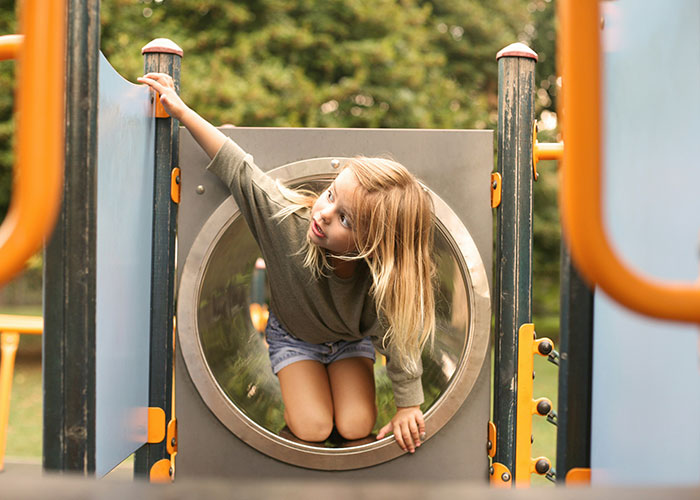Young girl showing quick reactions while playing on playground equipment outdoors in a park setting.
