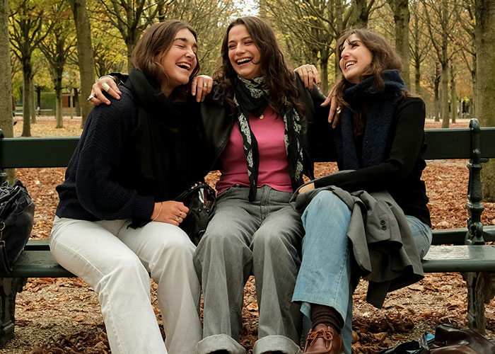 Three young women sitting on a park bench, laughing and enjoying a moment of quick reactions preventing a tragedy.