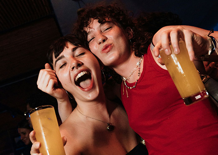 Two friends joyfully celebrating with drinks, showcasing quick reactions that prevented a tragedy in a lively setting.